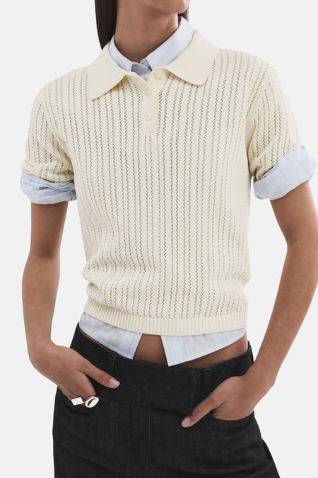 Polo beige en maille ajourée de MANGO, porté sur une chemise rayée et un pantalon taille basse.