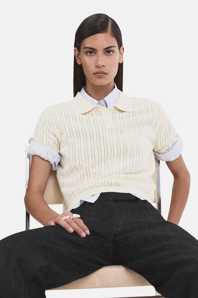 Beige polo van MANGO met ajourwerk, gedragen over een blauw gestreept overhemd en een donkere broek.