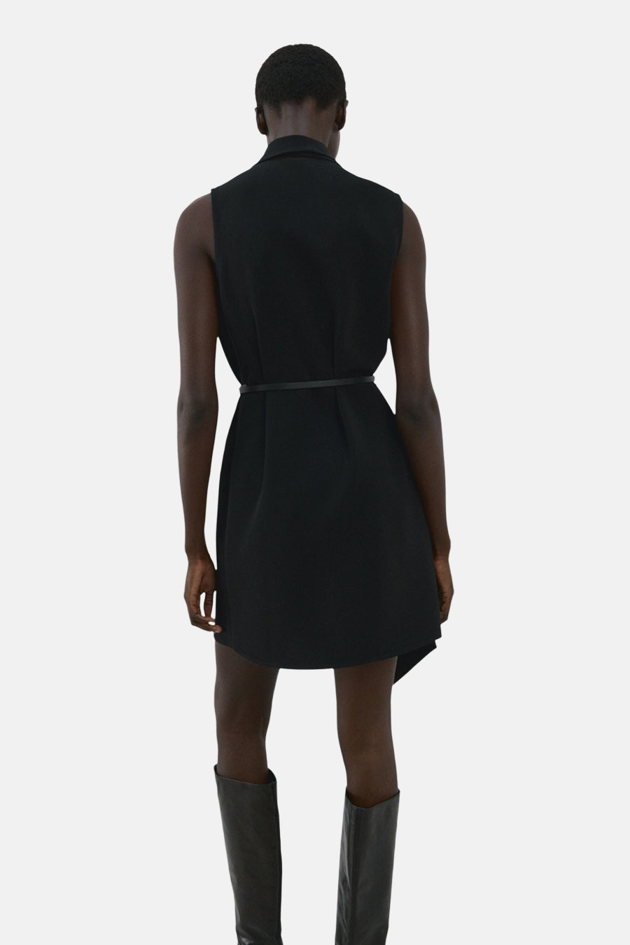 Robe noire de MANGO, avec ceinture fine, longueur au-dessus du genou, portée avec des bottes hautes noires.