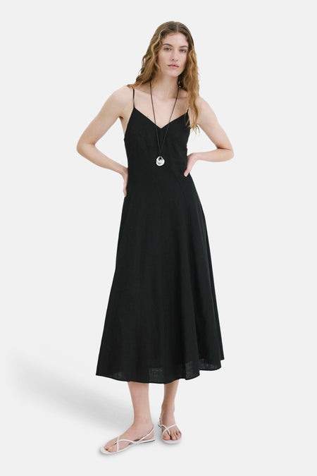 Robe noire de MANGO, coupe midi évasée, avec fines bretelles et un collier argenté.