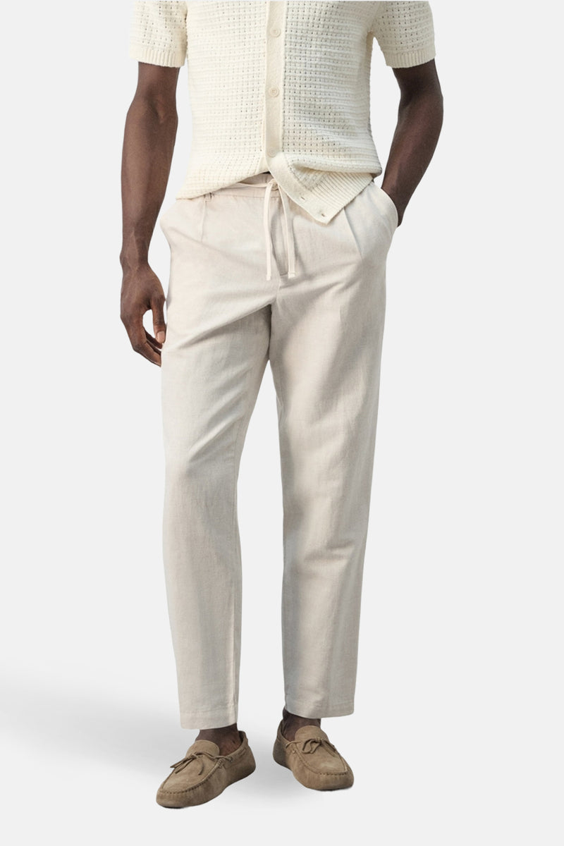Ecru broek van MANGO, gecombineerd met een gebreid vest met ajourpatroon en bruine loafers.