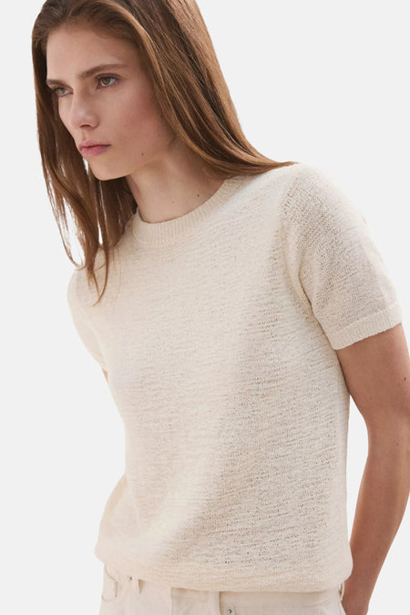 Beige MANGO pull met fijne breistructuur en korte mouwen, achterkant, gedragen met een gebroken witte wijde broek en zwarte sandalen.