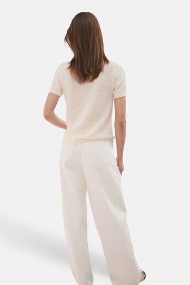 Pull col O beige de MANGO en maille fine et manches courtes, vue arrière, porté avec un pantalon ample blanc cassé et des sandales noires.