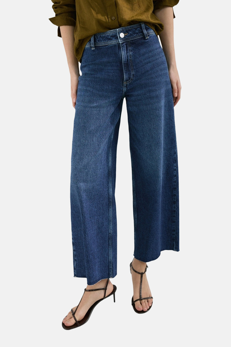 Jean large en denim bleu moyen de MANGO, porté avec un haut olive et des sandales minimalistes.