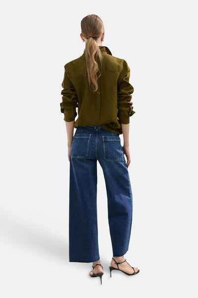 Jean large bleu moyen de MANGO, porté avec une chemise kaki et des talons aiguilles noirs.
