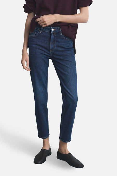 Jean Mom en denim bleu foncé de MANGO, porté avec un pull bordeaux et des chaussures noires.
