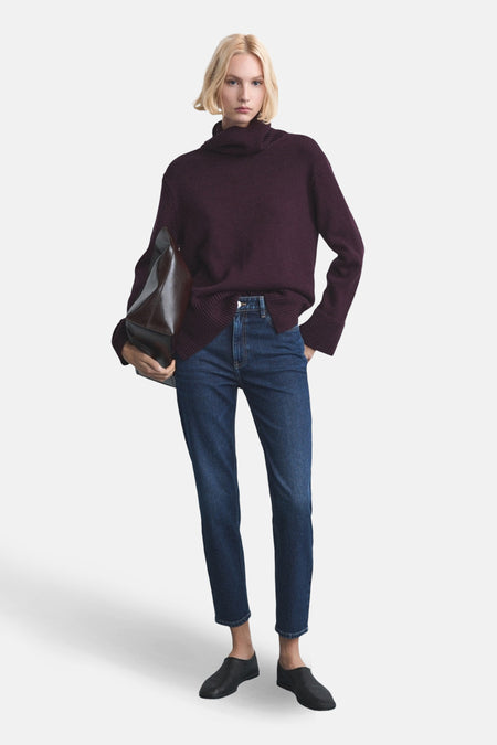 Jean Mom en denim bleu foncé de MANGO, porté avec un pull bordeaux à col roulé et des chaussures noires.