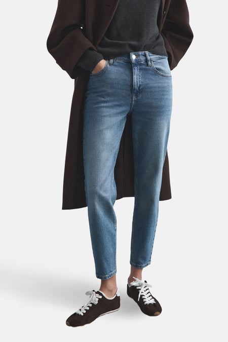 Jean Mom en denim bleu moyen de MANGO, porté avec un manteau marron et des baskets marron.