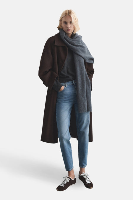 Jean Mom bleu moyen en denim - de MANGO - porté avec un manteau marron, un pull gris et une écharpe.