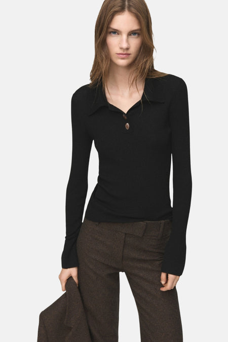 Pull noir à col rond de MANGO, en maille côtelée, porté avec un pantalon marron.
