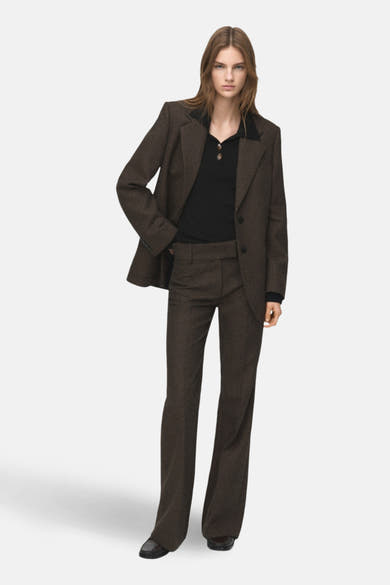 Zwarte rondehals trui van MANGO, gedragen onder een getextureerde bruine blazer en een bijpassende broek.
