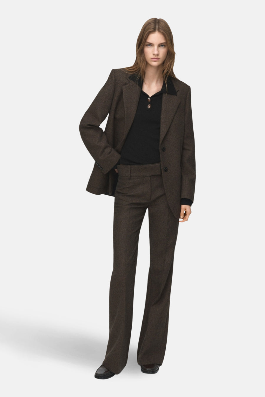 Zwarte rondehals trui van MANGO, gedragen onder een getextureerde bruine blazer en een bijpassende broek.