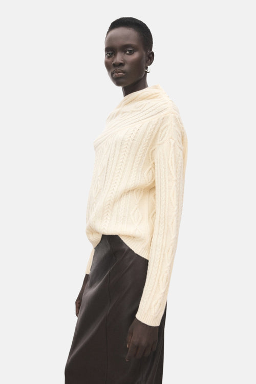 Pull à col rond écru de MANGO, avec texture torsadée et porté avec une jupe noire.