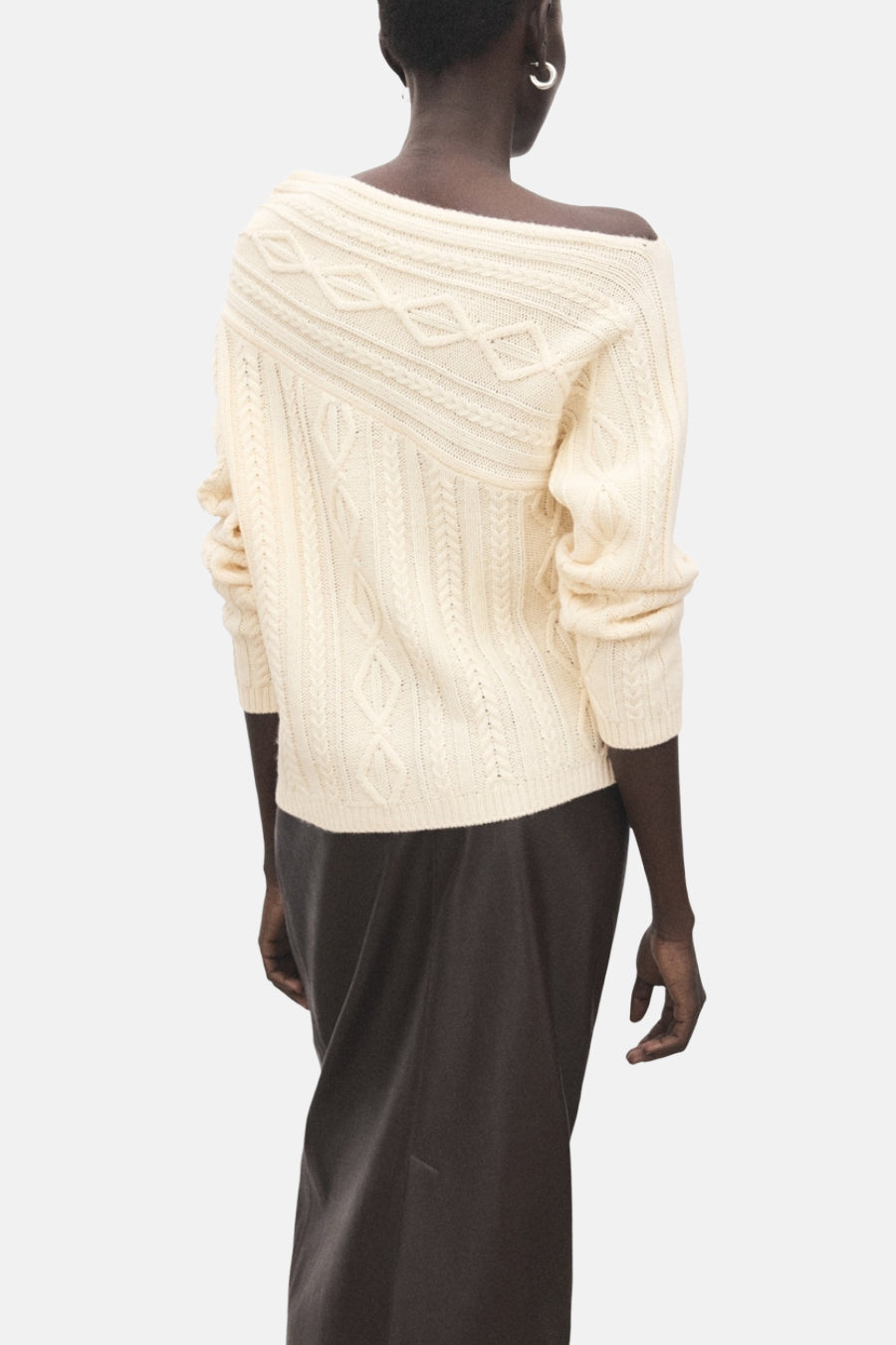Pull écru à col rond de MANGO, avec motif torsadé sur le devant et manches longues, porté avec une jupe longue sombre.
