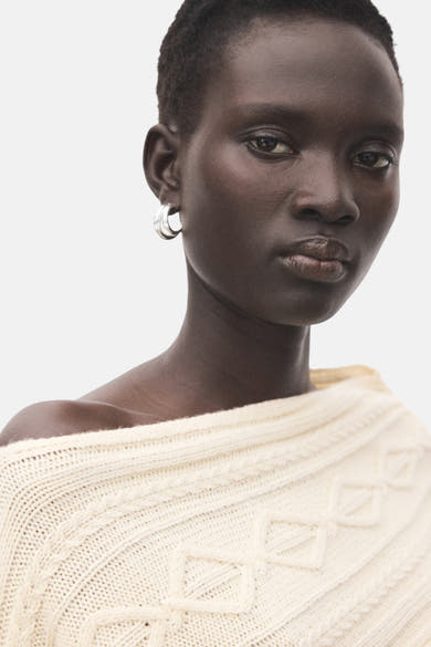 Pull à col rond écru de MANGO, avec texture en maille torsadée et col bateau asymétrique porté par un modèle.