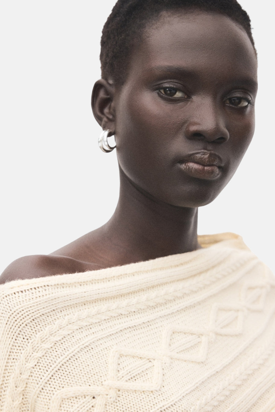 Pull à col rond écru de MANGO, avec texture en maille torsadée et col bateau asymétrique porté par un modèle.