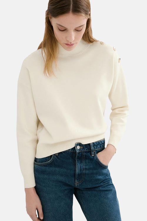 Pull à col rond écru de MANGO, orné de boutons décoratifs à l'épaule, porté avec un jean bleu.
