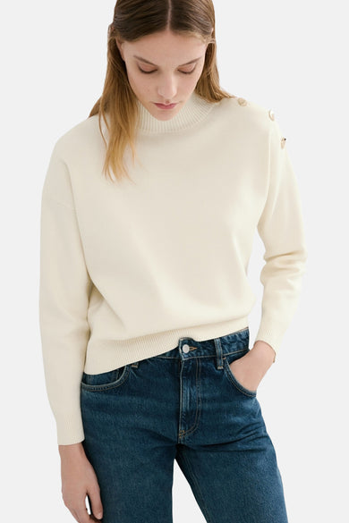 Pull à col rond écru de MANGO, orné de boutons décoratifs à l'épaule, porté avec un jean bleu.
