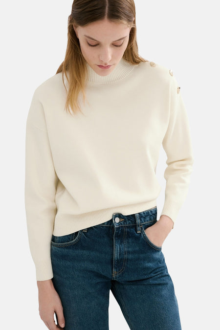 Pull à col rond écru de MANGO, orné de boutons décoratifs à l'épaule, porté avec un jean bleu.
