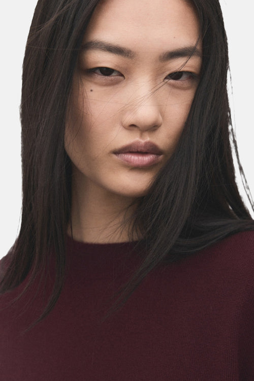 Pull à col rond bordeaux de MANGO, porté par un mannequin aux cheveux noirs lisses.