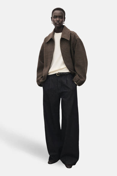 Ecru ronde hals trui van MANGO, gedragen met een bruin geruit jasje en een zwarte wijde broek met riem.