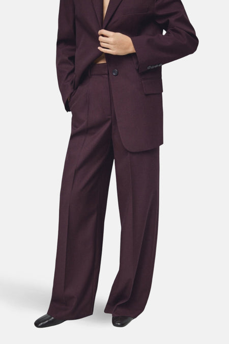 Pantalon de costume bordeaux de MANGO, coupe ample, porté avec un blazer assorti et des chaussures noires.
