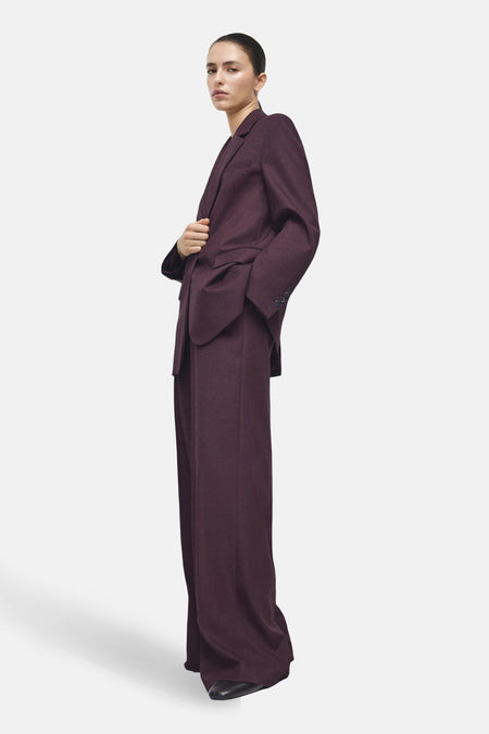 Pantalon de costume bordeaux par MANGO, coupe ample et jambes longues, porté avec un blazer assorti.