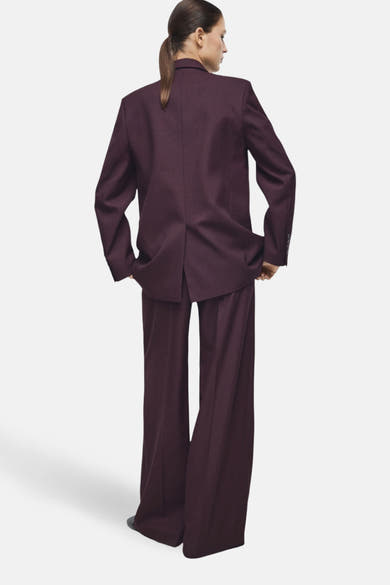 Pantalon de costume bordeaux de MANGO, coupe ample et jambes larges, porté avec une veste assortie.