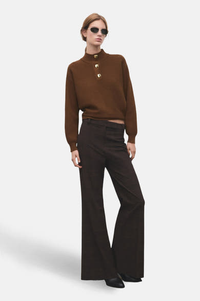 Pull à col roulé brun de MANGO, avec boutons dorés décoratifs sur le col montant, porté avec un pantalon évasé.