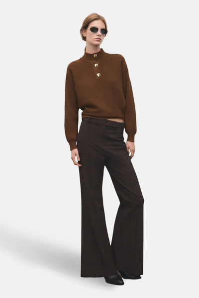 Pull à col roulé brun de MANGO, avec boutons dorés décoratifs sur le col montant, porté avec un pantalon évasé.