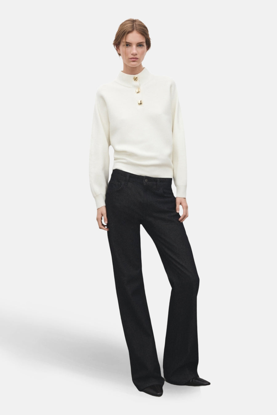 Pull à col roulé écru de MANGO, orné de boutons dorés, porté avec un jean foncé bootcut.