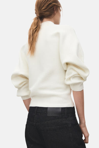 Pull à col roulé écru de MANGO, porté avec un jean noir, vue de dos et manches bouffantes.
