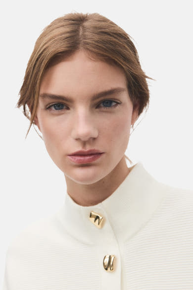Pull à col roulé écru de MANGO, avec boutons dorés décoratifs et texture côtelée discrète.