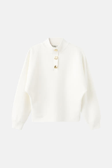 Pull col roulé écru de MANGO, avec trois boutons dorés et une texture côtelée.
