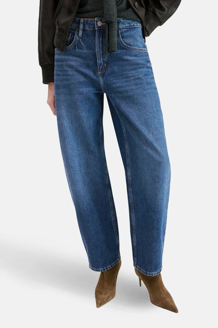 Jean ample bleu moyen de MANGO, porté avec des bottines marron en daim et une veste noire.