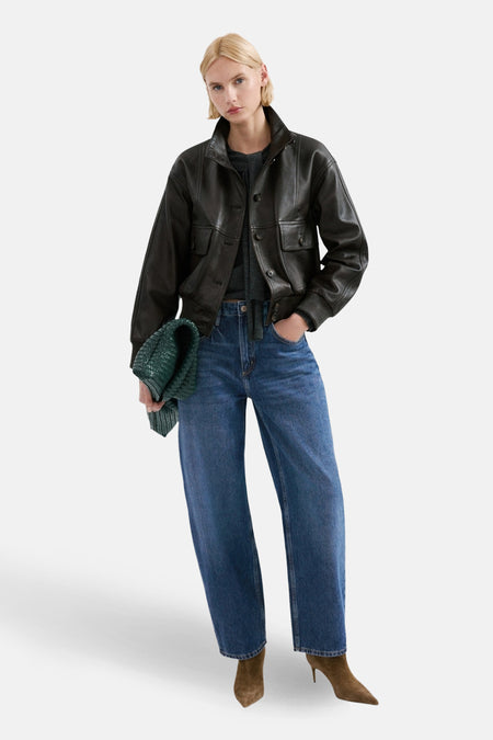 Jean en denim bleu moyen de MANGO, porté avec une veste en cuir marron, un haut gris et des bottines marron.
