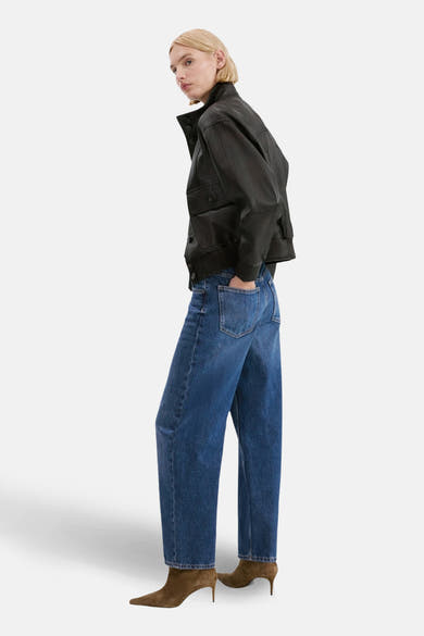 Jean bleu moyen BET de MANGO, porté avec une veste en cuir noir et des bottines marron.