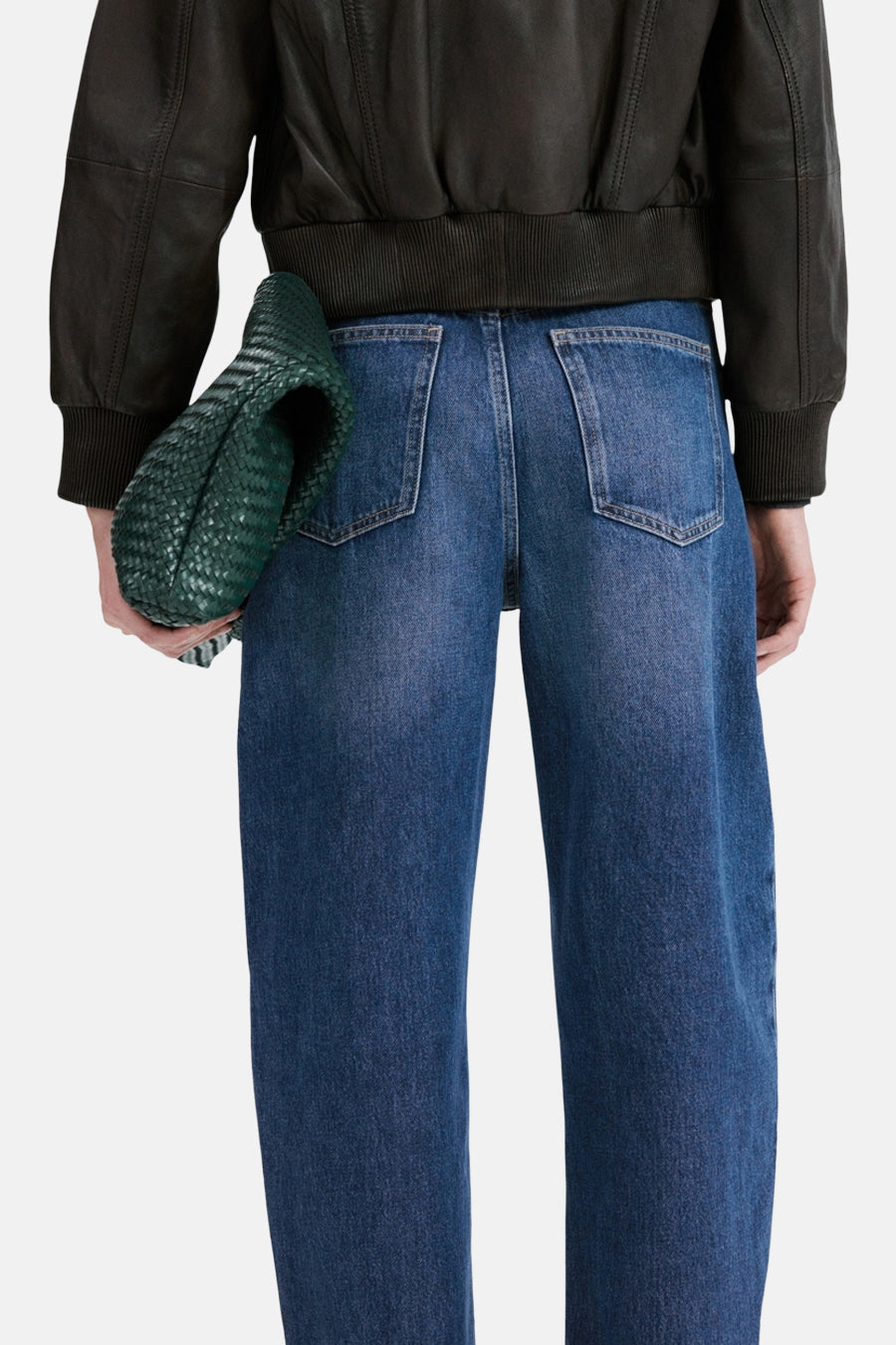 Middelblauwe spijkerbroek van MANGO, met achterzakken, gedragen met een leren jasje en een groene clutch.