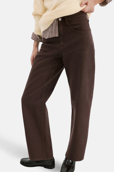 Jean coloré brun par MANGO, coupe droite, porté avec un pull jaune et des mocassins noirs.