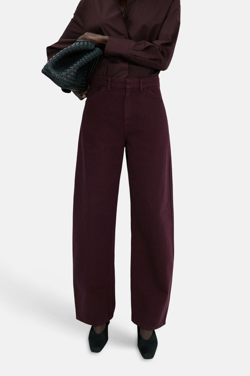 Jeans coloré bordeaux de MANGO, à jambes larges, porté avec une chemise assortie et un sac à main noir tressé.