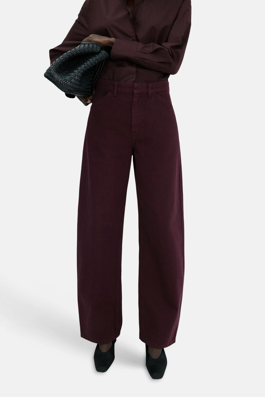 Jeans coloré bordeaux de MANGO, à jambes larges, porté avec une chemise assortie et un sac à main noir tressé.