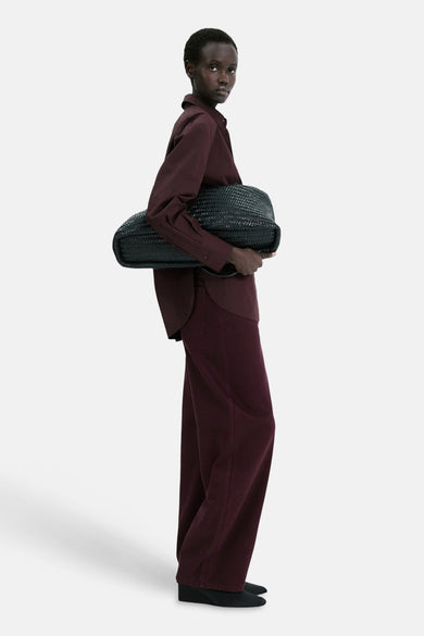 Jean coloré bordeaux de MANGO, porté avec une chemise bordeaux et un sac tressé noir.