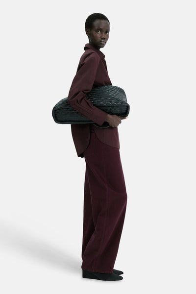 Jean coloré bordeaux de MANGO, porté avec une chemise bordeaux et un sac tressé noir.