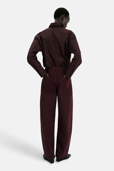 Jean coloré bordeaux de MANGO, coupe ample, avec les mains dans les poches arrière et chaussures noires.