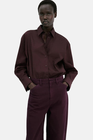 Jeans colorés bordeaux de MANGO, portés avec une chemise boutonnée de couleur similaire et mains dans les poches.