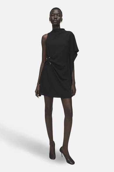 Zwarte asymmetrische jurk van MANGO, met draperie aan de taille en minimalistische afwerkingen, gedragen met klassieke zwarte pumps.