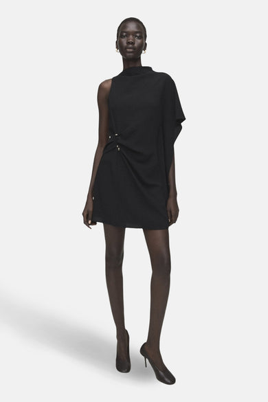Robe noire asymétrique de MANGO, avec drapé à la taille et finitions minimalistes, portée avec des escarpins noirs classiques.
