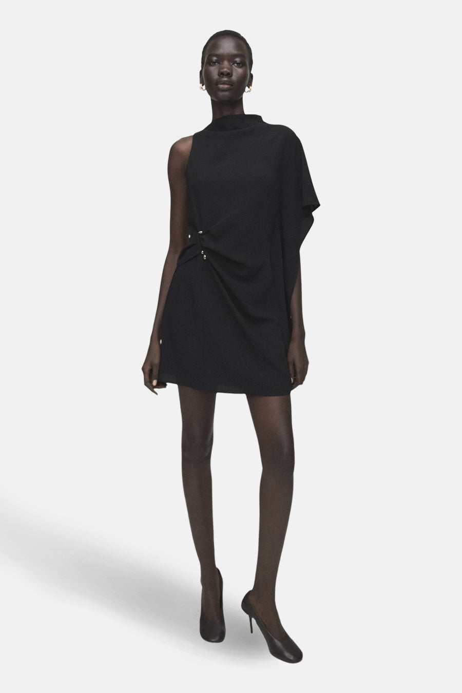 Zwarte asymmetrische jurk van MANGO, met draperie aan de taille en minimalistische afwerkingen, gedragen met klassieke zwarte pumps.