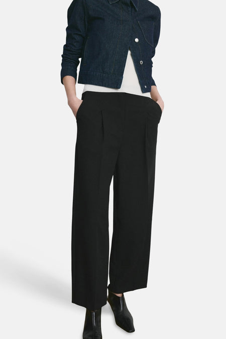 Pantalon noir de MANGO, coupe ample avec des plis, porté avec une veste en jean et des bottines noires.
