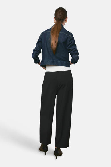 Pantalon noir de MANGO, coupe ample, porté avec une veste en jean courte et des chaussures à talons aiguilles.